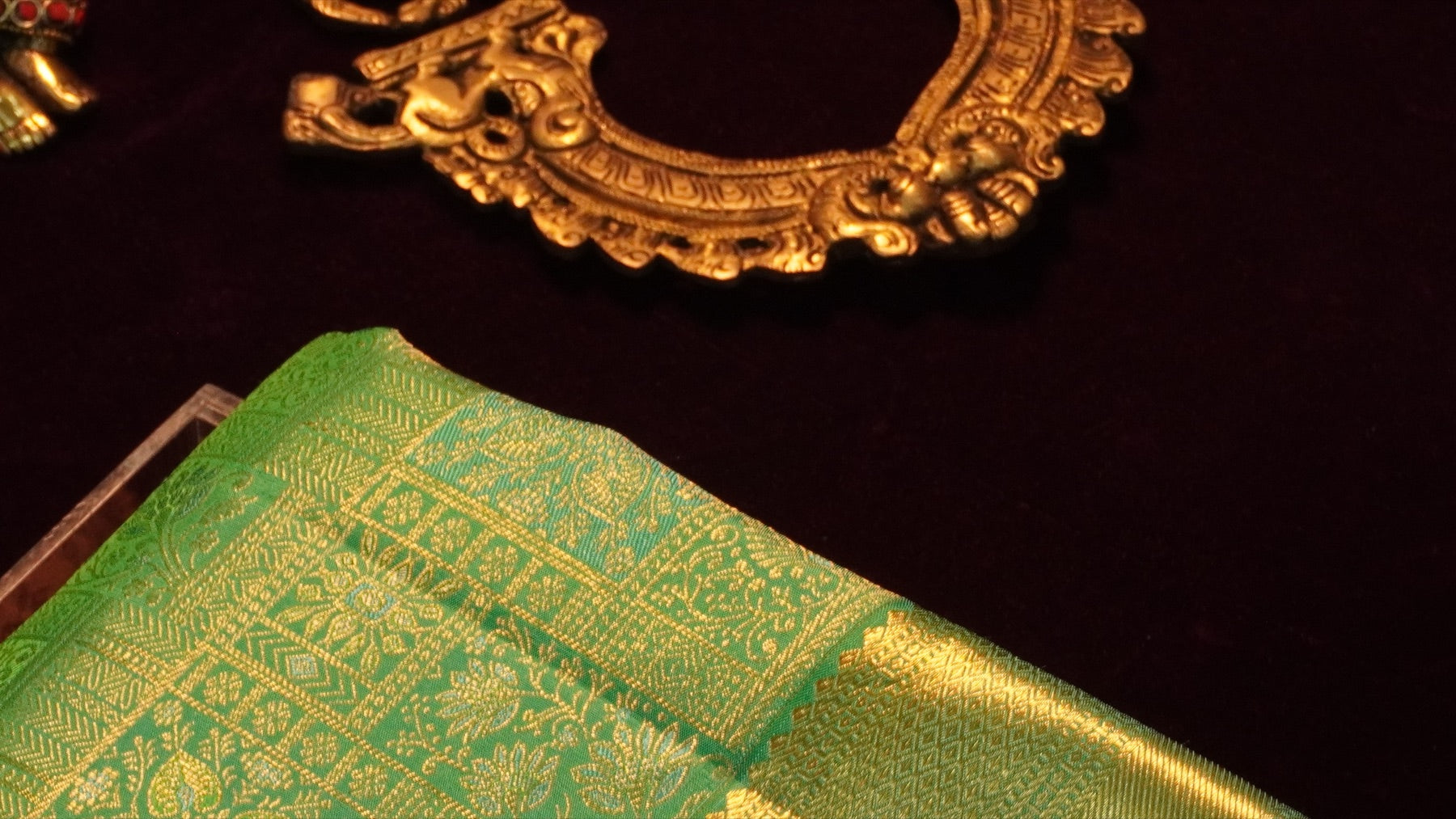Green silk saree with gold zari and a traditional brass mirror
